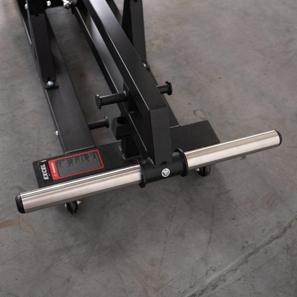 Close-up of the base of a black fitness machine with a silver bar and wheels on a concrete floor.
