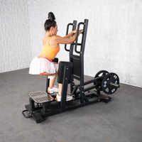 Thumbnail for Woman using a black standing hip abductor machine with plate weights, holding handles and pressing legs outwards.