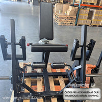 Thumbnail for Black plate-load leg extension machine with padded seat and backrest, on a wooden pallet in a warehouse.
