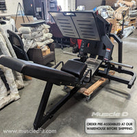 Thumbnail for Black plate-loaded leg press machine with padded seat and backrest in a warehouse setting.