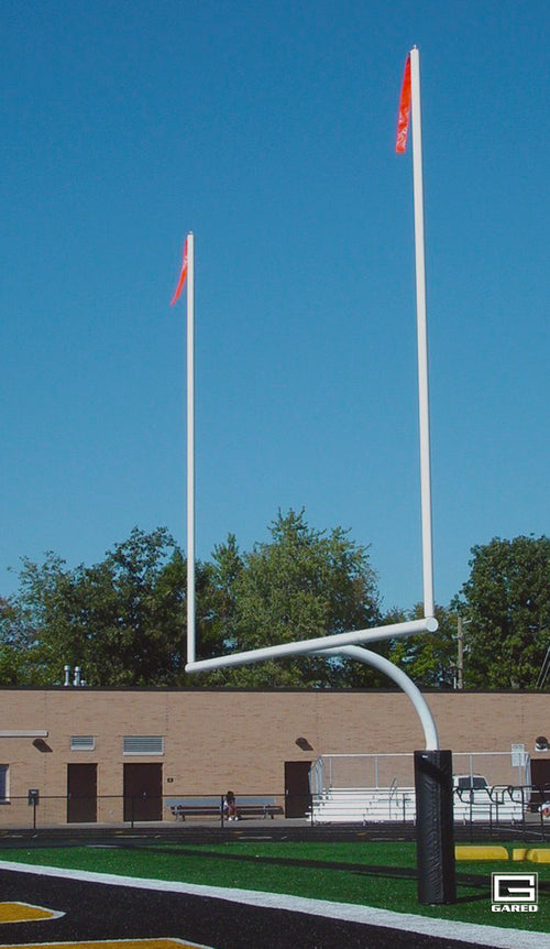 White football goalpost with red flags on a green field under a blue sky.