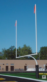 White football goalpost with red flags on a field with a building and trees in the background.
