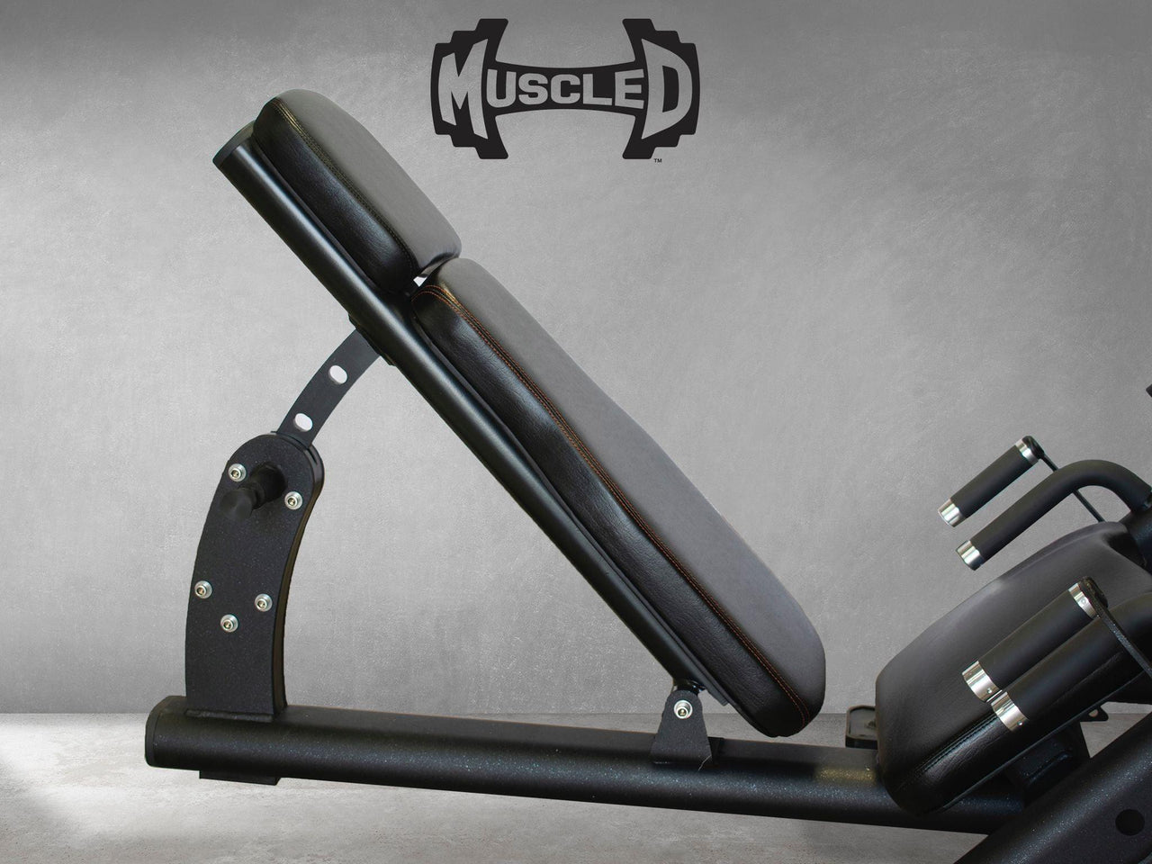 Black leg press machine with an adjustable back pad and handles, against a gray wall.