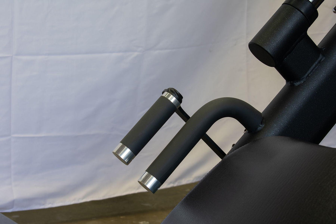 Close-up of black leg press machine handles with silver ends and a black padded seat.