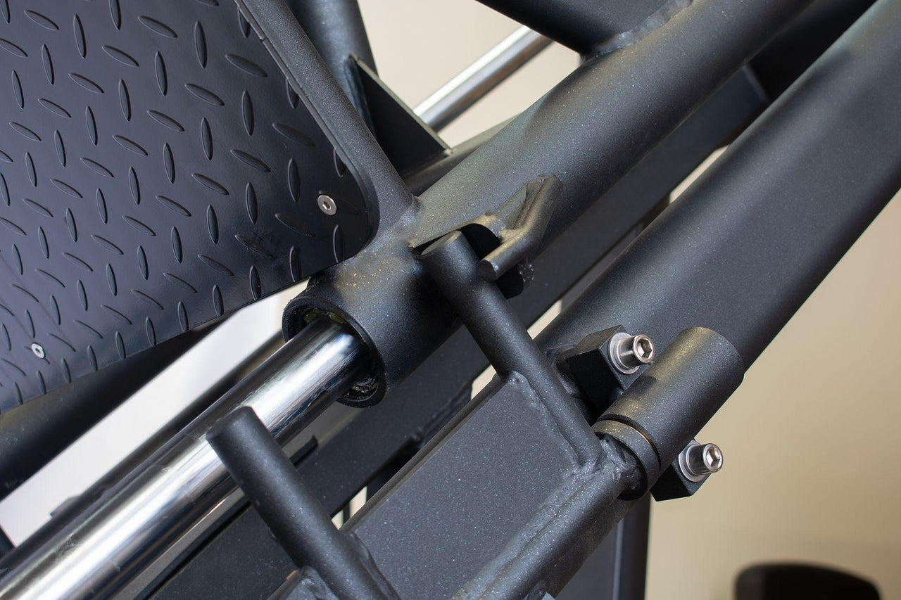 Close-up of a leg press machine's textured footplate and black metal frame with chrome rails.