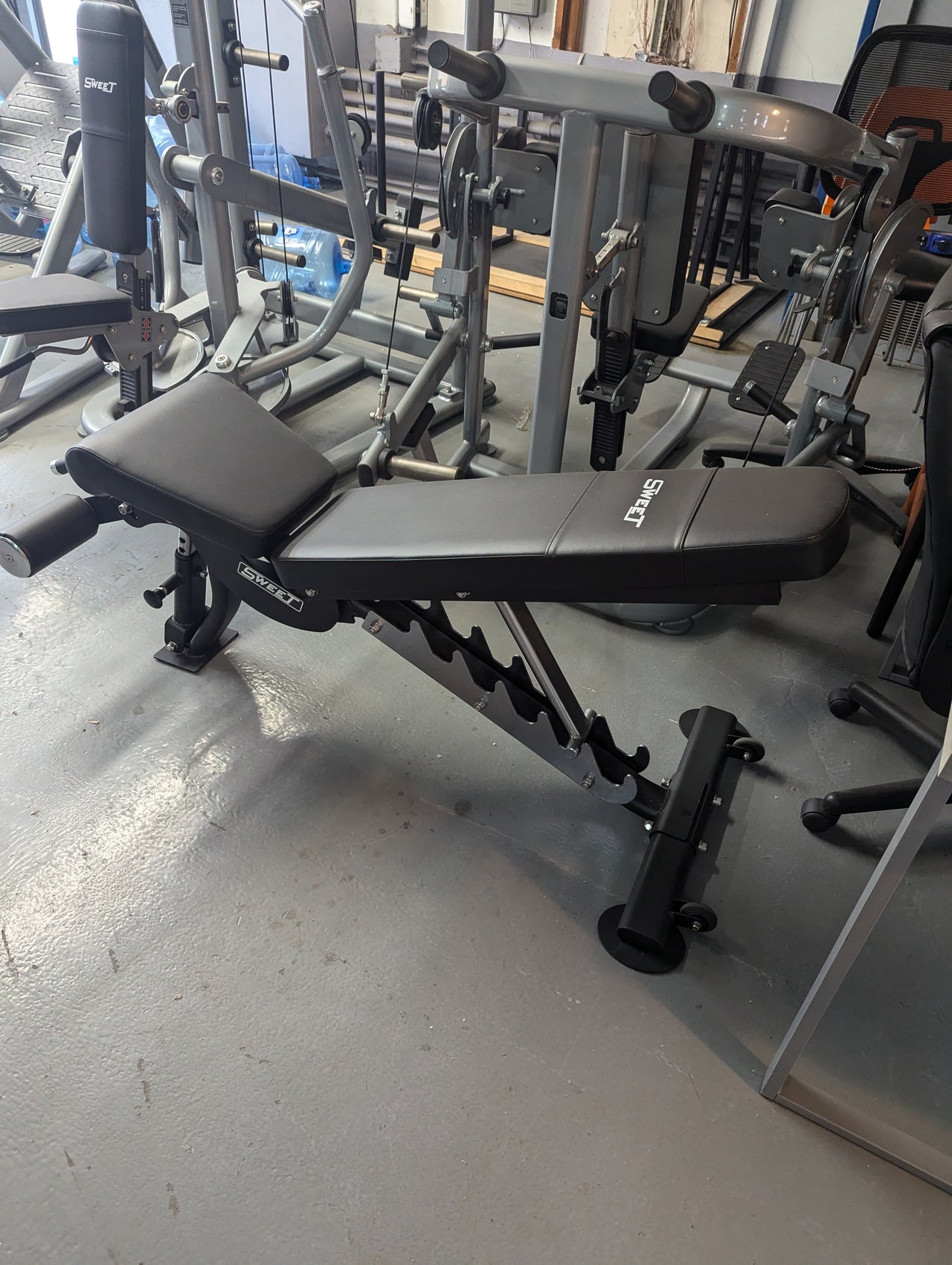 Black adjustable weight bench with Sweet logo in a gym setting.