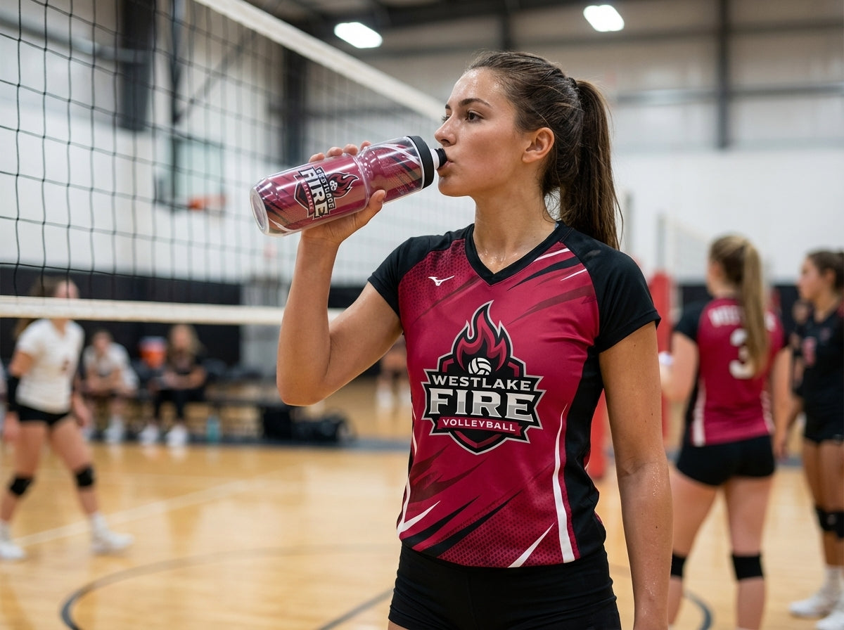Volleyball player in a red jersey drinking from a custom "Westlake Fire" water bottle on a court.