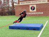 Blue football crash pad on turf as a player in a black and red uniform dives toward it