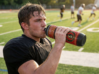 Thumbnail for Sweaty football player in black jersey drinking from a red and black custom water bottle on a field.