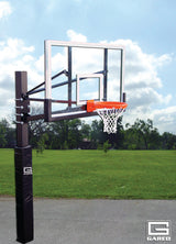 Basketball hoop with clear backboard, orange rim, and white net on a black pole with padding, outdoors.