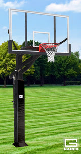 Adjustable basketball hoop with clear acrylic backboard and red rim, on a grassy field with trees.