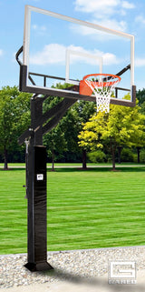 Adjustable basketball hoop with a clear glass backboard and orange rim, on a grassy field.