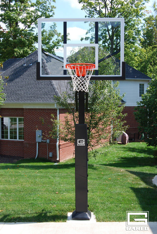 Adjustable basketball hoop with clear acrylic backboard and orange rim in a backyard setting.
