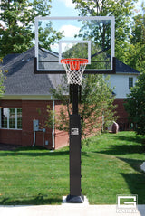 Adjustable basketball hoop with a clear glass backboard and orange rim in a backyard.