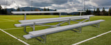 Three-row aluminum bleacher on a green sports field with white lines, mountains and trees in the background.