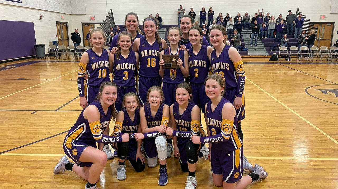A basketball team of girls and young women in purple and gold uniforms, some wearing arm sleeves.