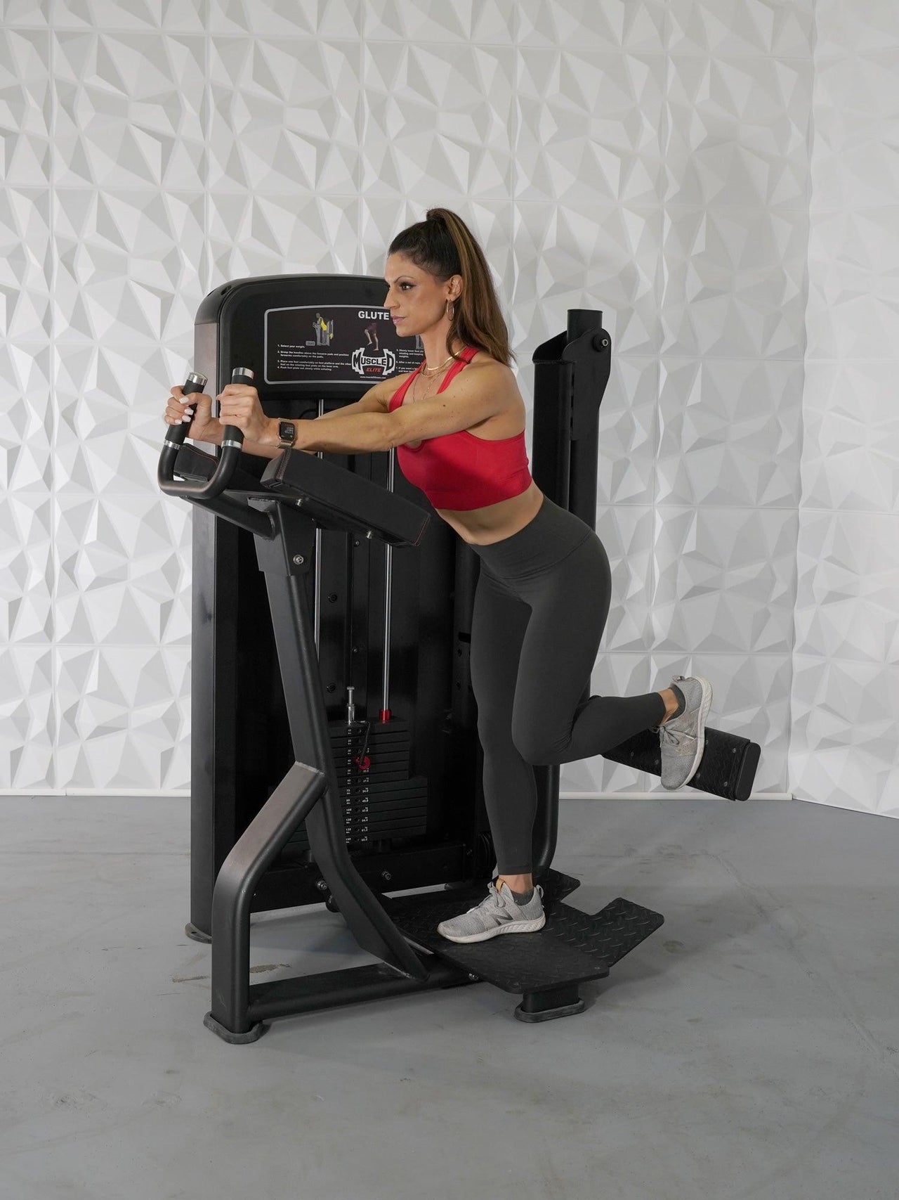 Woman in red top and gray leggings using a black glute exercise machine.