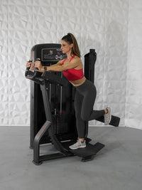 Thumbnail for Woman in red top and gray leggings using a black glute exercise machine.