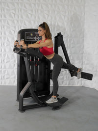 Thumbnail for Woman in red top and gray leggings using a black glute exercise machine.