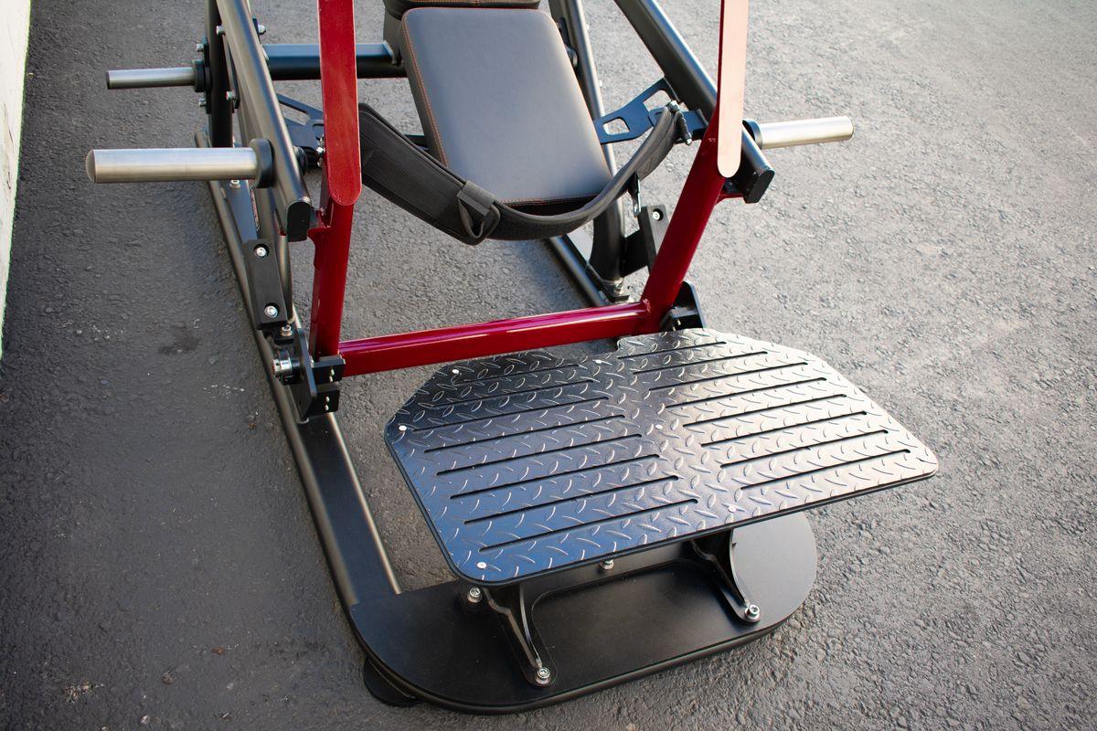 Close-up of a hip thruster machine with a black footplate, red frame, and padded seat.