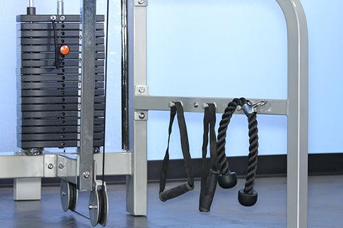 Close-up of a gym machine with a weight stack, pulleys, and two black cable attachments hanging on a bar.