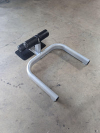 Thumbnail for Sissy squat machine with a gray frame, black footplate, and black padded leg rests on a concrete floor.