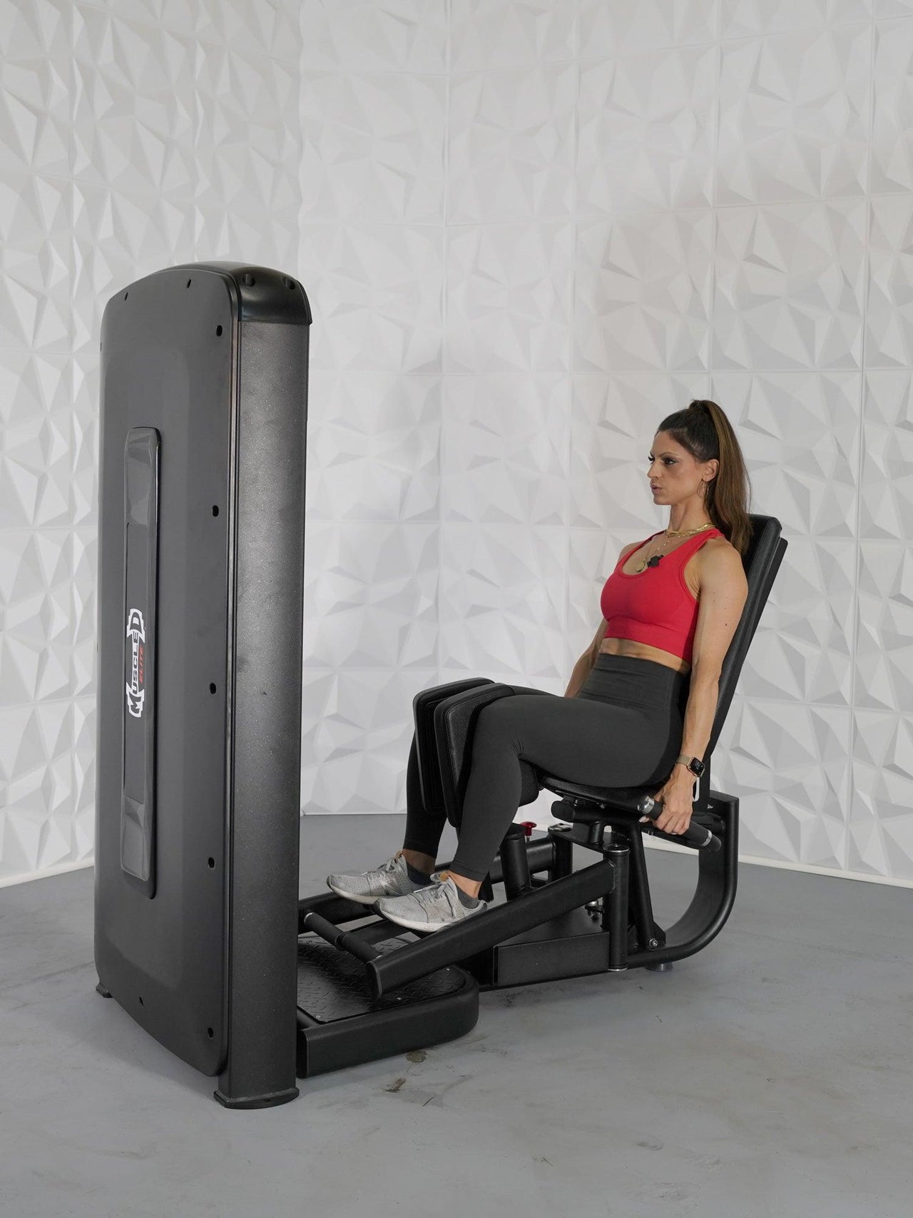 Woman in red top and black leggings using a black inner and outer thigh exercise machine.