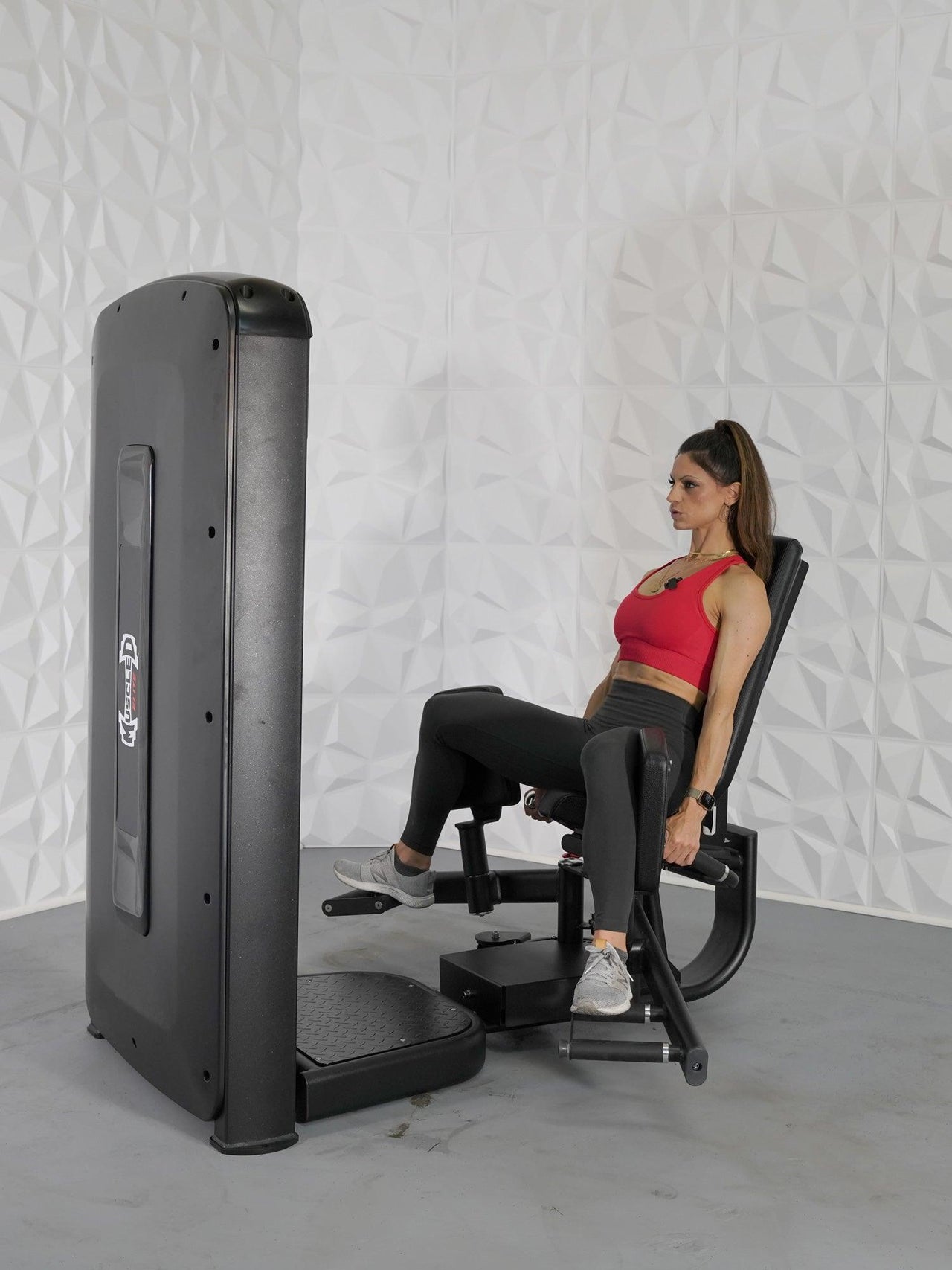 Woman in red top and black leggings using a black inner/outer thigh workout machine.