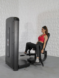 Thumbnail for Woman in red top and black leggings using a black inner/outer thigh workout machine.
