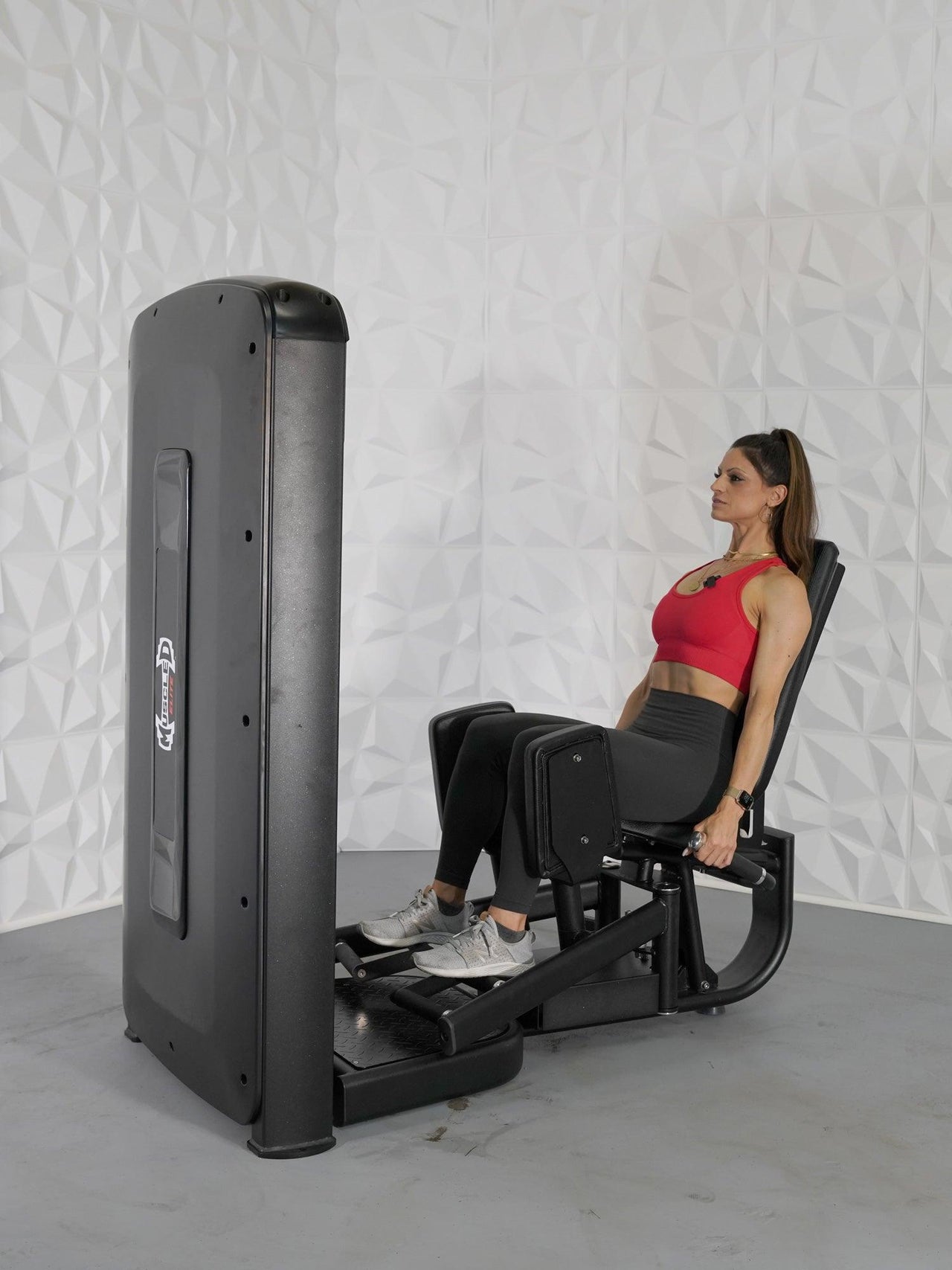 Woman in red top and black leggings using a black inner and outer thigh workout machine.