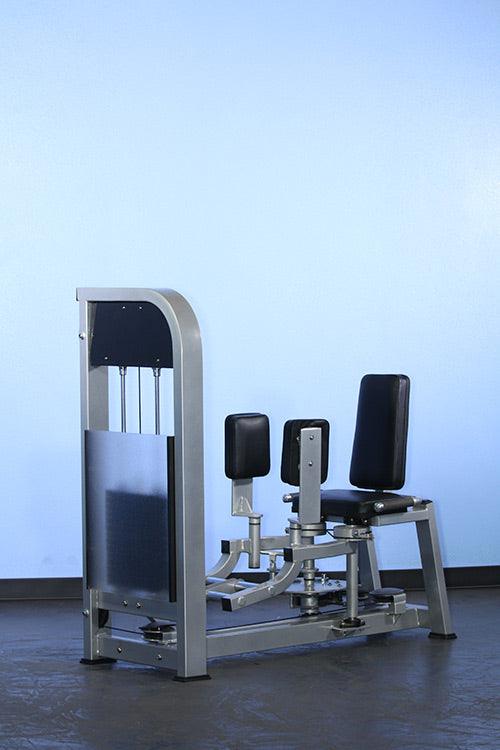 Seated inner-outer thigh combo machine with black pads and silver frame against a light blue wall.