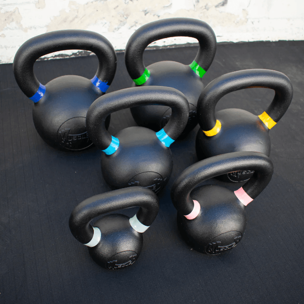 Six black kettlebells with colored bands on handles, on a dark surface.