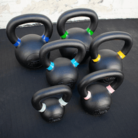 Thumbnail for Six black kettlebells with colored bands on handles, on a dark surface.