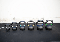 Thumbnail for Six black kettlebells of varying sizes with colored bands on handles, arranged on a black mat.