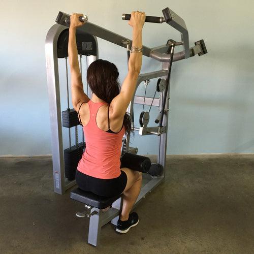 Woman using a lat pulldown machine, viewed from behind, arms extended upward holding the bar.