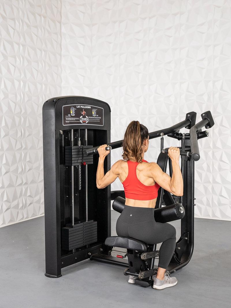 Woman in red top and black leggings using a black lat pulldown machine with weight stack.