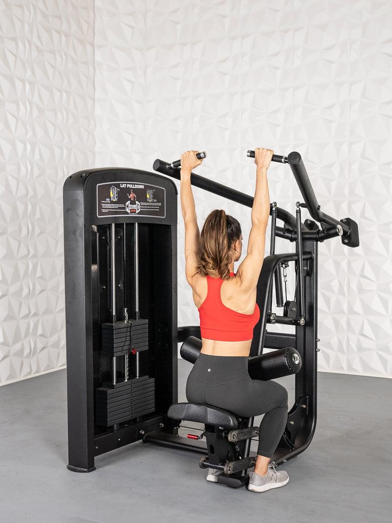 Woman in red top and black leggings using a black lat pulldown machine with weight stack.