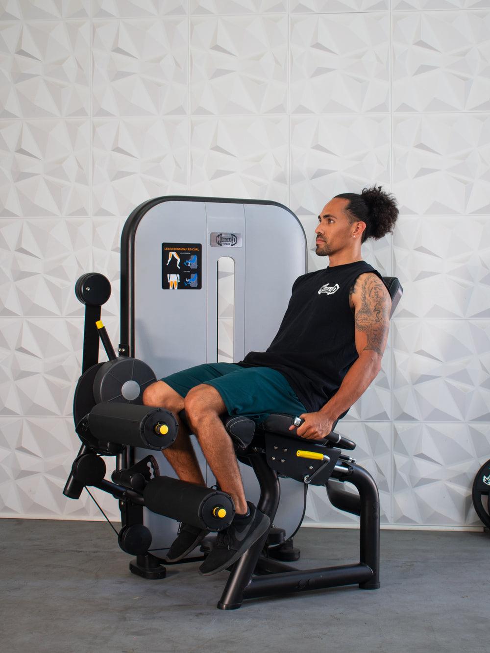 Man using a black and gray leg extension/curl machine with yellow accents.