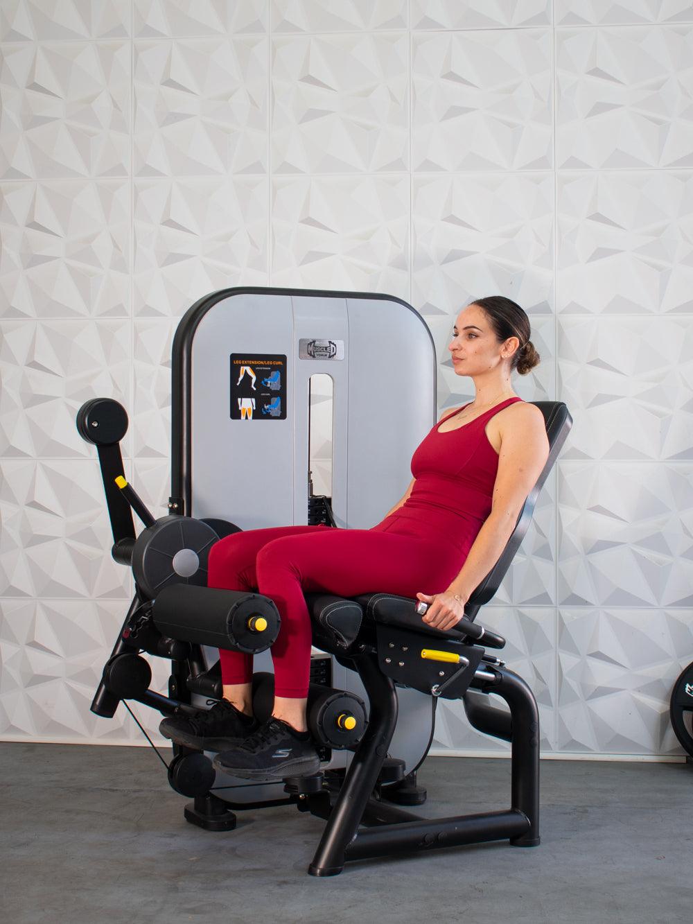 Woman in red using a leg extension/curl machine, performing a leg extension.