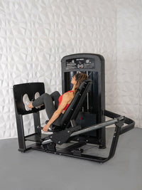 Thumbnail for Woman using a black selectorized leg press machine with a white textured wall background.