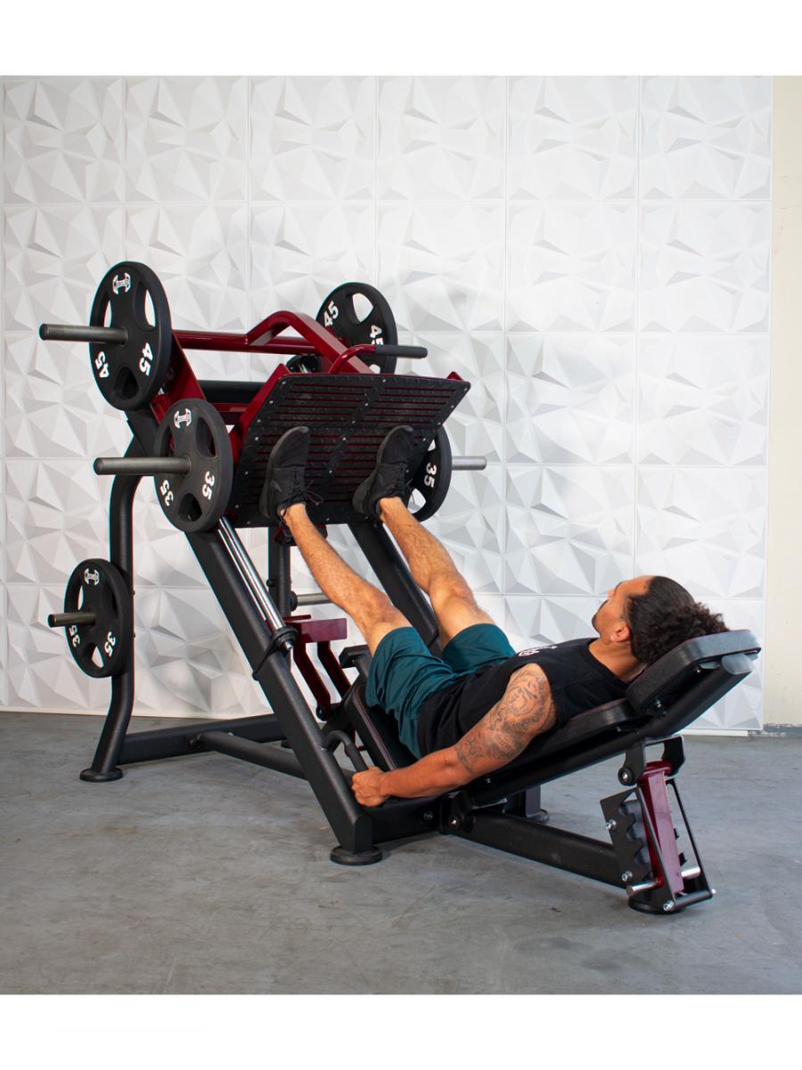 Man using a black and red leg press machine with weight plates in a gym.