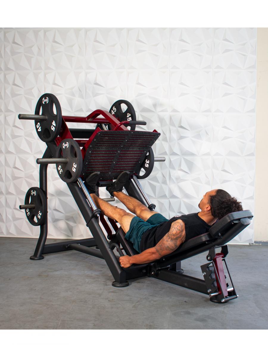 Man using a red and black plate-loaded leg press machine with weights in a gym.