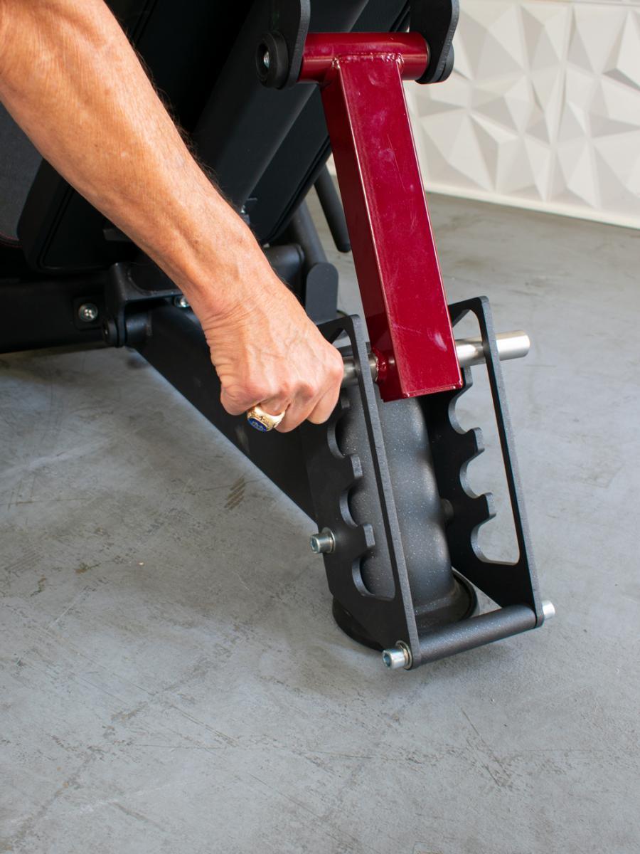 Hand adjusting the red and black leg press machine, showing the adjustable back pad mechanism.