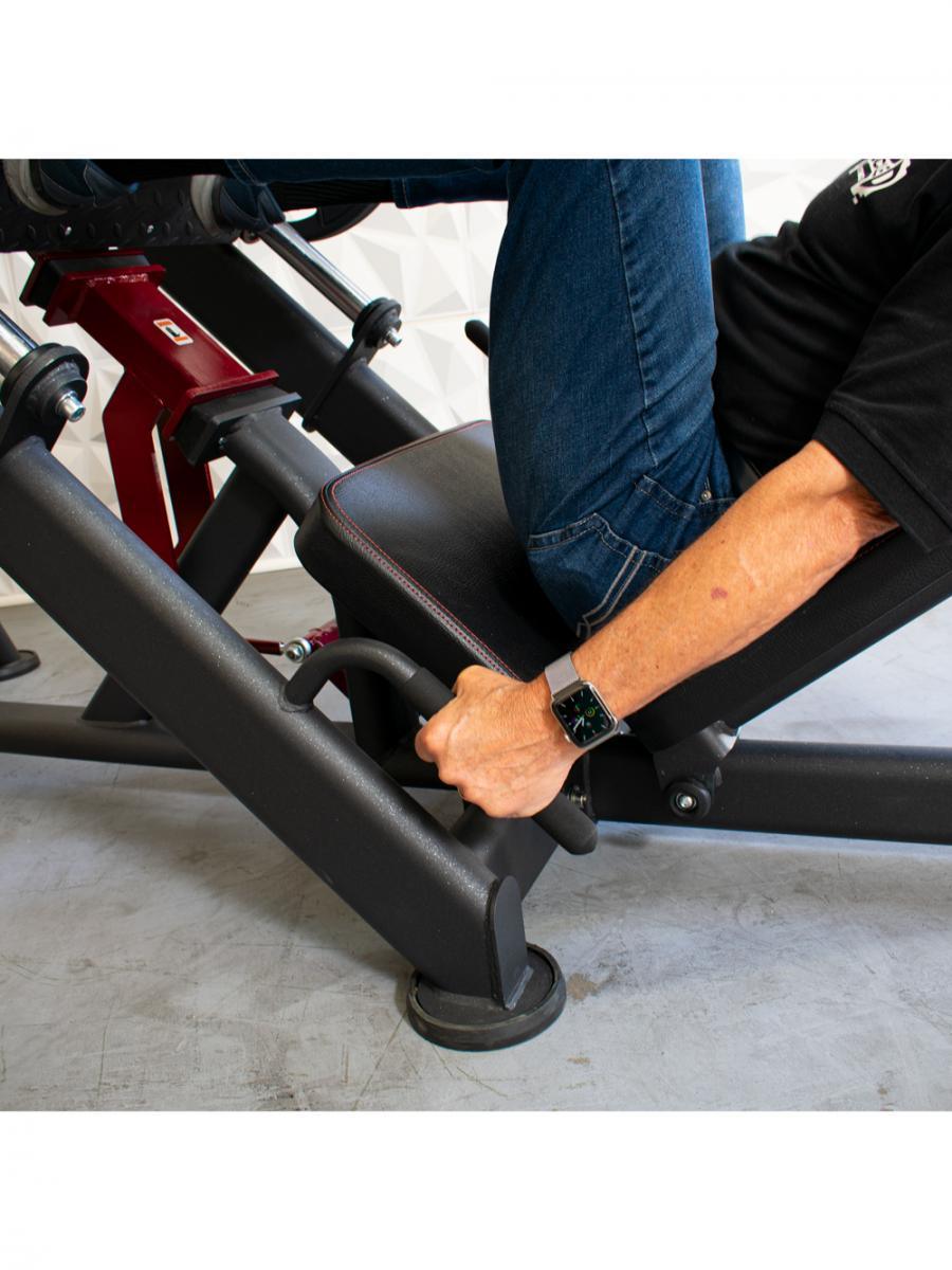 Person in jeans and black shirt using a leg press machine, holding onto handles.