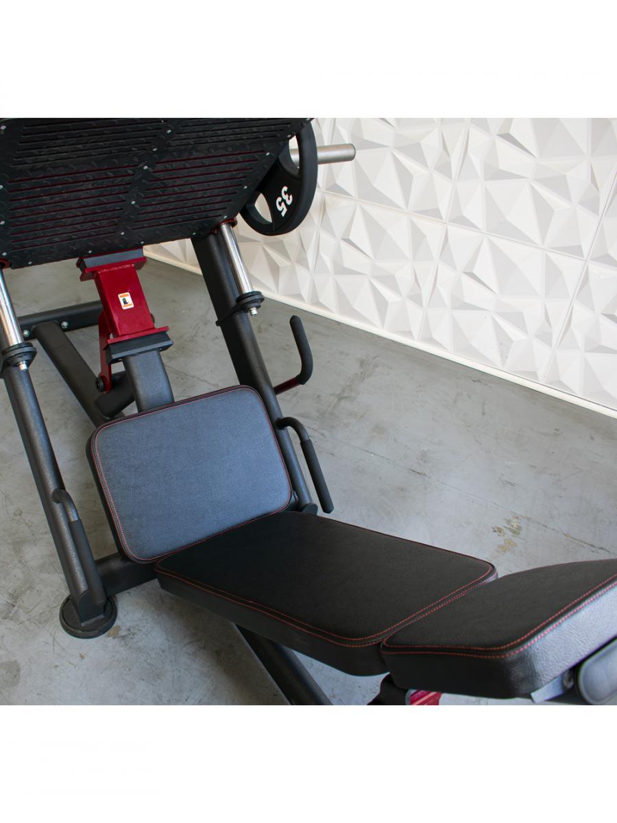 Black and red leg press machine with adjustable back pad and plate loaded weight, on a concrete floor.