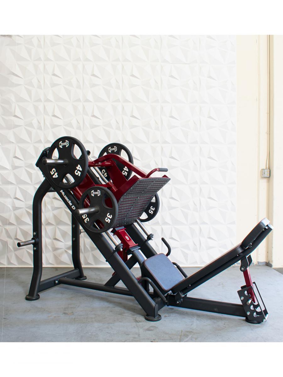 Red and black plate-loaded leg press machine with weight plates on a concrete floor.