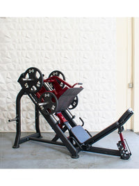 Thumbnail for Red and black plate-loaded leg press machine with weight plates on a concrete floor.