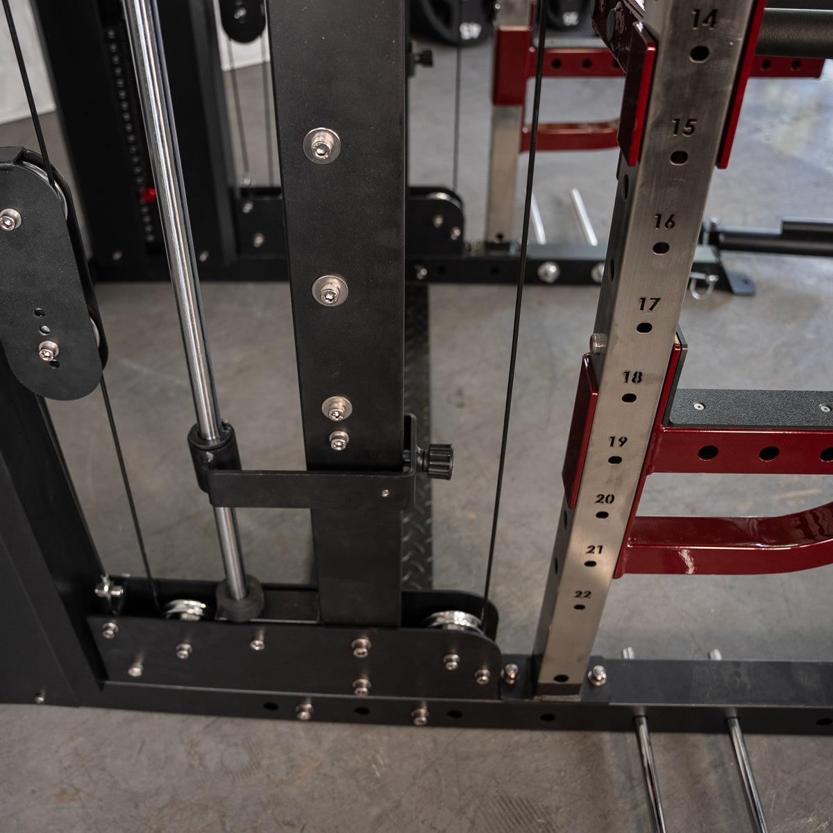 Close-up of a fitness machine's black and red frame, showing cables, pulleys, and numbered adjustment holes.