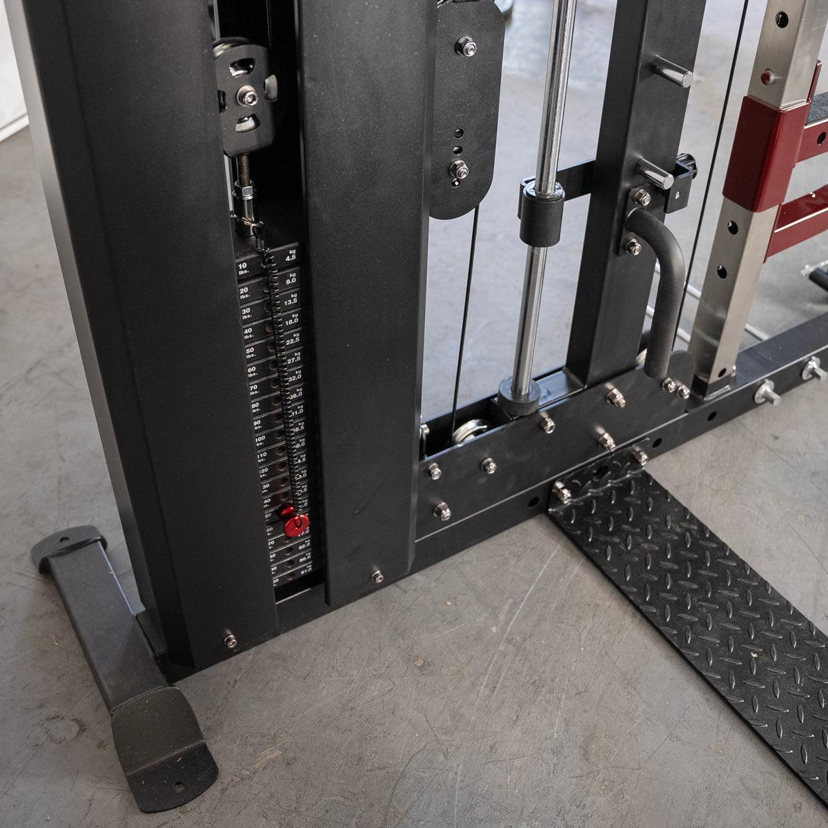 Close-up of a weight stack on a black fitness machine with a red weight pin and diamond plate footrest.