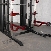 Thumbnail for Close-up of a black and red multi-gym machine with a barbell, safety arms, and weight plate storage.